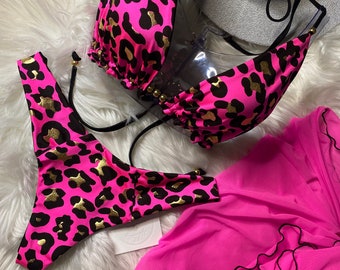 May include: A neon pink bikini set featuring a black and gold leopard print pattern, including a triangle top with gold bead accents and matching bottoms, paired with a sheer pink sarong skirt with a black lettuce edge trim detail.