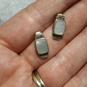 May include: A pair of silver earrings with a rectangular mother-of-pearl stone set in each earring. The earrings are surrounded by a border of small black stones.