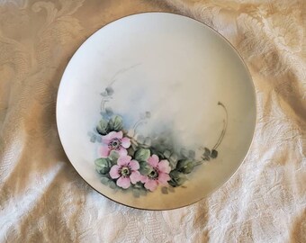 May include: A white porcelain plate with a gold rim features a hand-painted design of pink flowers and green leaves.
