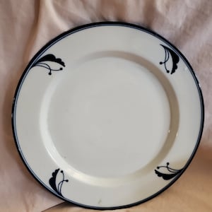 May include: A white ceramic dinner plate with a blue rim and black floral designs.