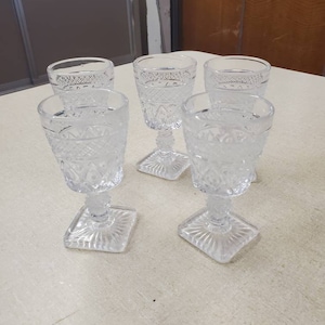 Puede incluir: Cinco copas de vidrio transparente con un diseño de vidrio cortado y bases cuadradas.