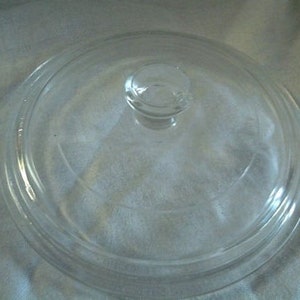 Op de afbeelding: Een heldere glazen deksel met een ronde vorm en een kleine, afgeronde handgreep. De deksel heeft een licht verhoogde rand en is ontworpen voor gebruik op een pot of pan. Het glas is transparant, waardoor de inhoud zichtbaar is.