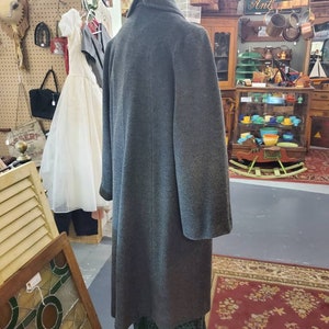 May include: A gray wool coat with a high collar and long sleeves. The coat is on a mannequin in a shop setting.