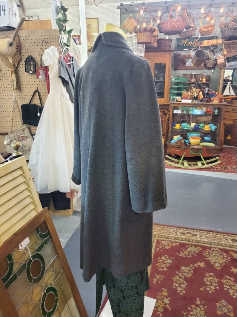May include: A gray wool coat with a high collar and long sleeves. The coat is on a mannequin in a shop setting.