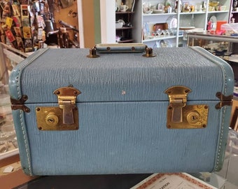 May include: A vintage blue suitcase with brass hardware and a textured fabric exterior. The suitcase has two latches and a handle on the top.