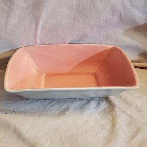 Puede incluir: Un plato de servir rectangular de cerámica azul claro con un interior rosa. El plato es rectangular con bordes ligeramente redondeados.