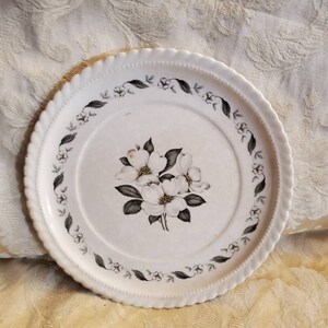 Puede incluir: Plato de cerámica blanco con un diseño floral en blanco y negro. El plato tiene un borde festoneado y un borde de pequeñas flores blancas y negras.