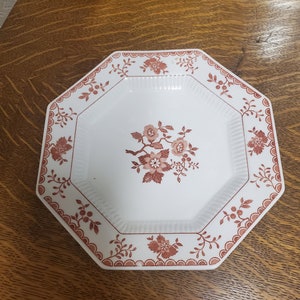 Puede incluir: Plato octogonal blanco con un diseño floral rojo. El plato tiene un borde festoneado y un borde elevado.