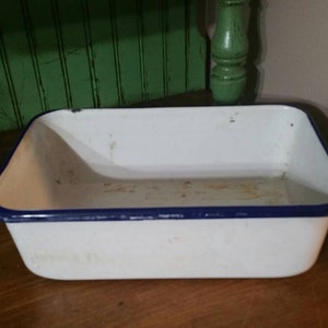 May include: White enamel baking dish with a blue rim. The dish is slightly dirty and has a few scratches.