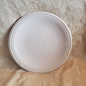 Puede incluir: Un plato de cerámica blanco con un borde elevado. El plato es redondo y tiene una superficie lisa.