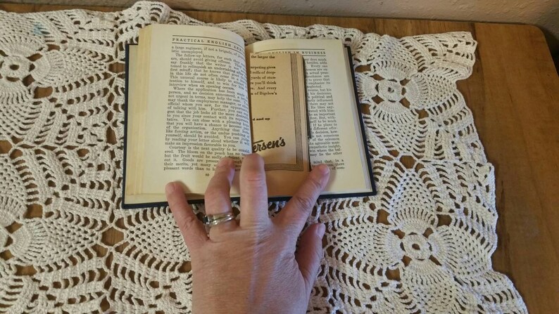 May include: An open book with a black cover and white pages. The book is titled "Practical English for Business". The pages are open to a section on "The Importance of Truthfulness". A hand is holding the book open.