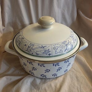 May include: White enamel pot with a blue and green floral design. The pot has a lid with a white knob.