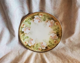 May include: A white porcelain plate with a gold rim and a floral design of pink roses and green leaves.
