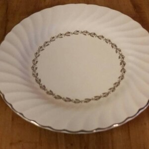 May include: White ceramic plate with a gold rim and a gold leaf design around the edge.