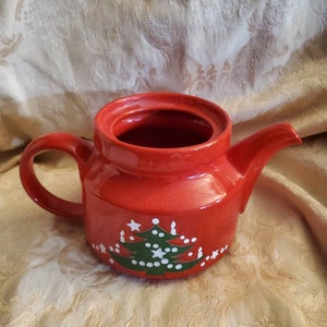 May include: Red ceramic teapot with a green Christmas tree design and white stars and candles.