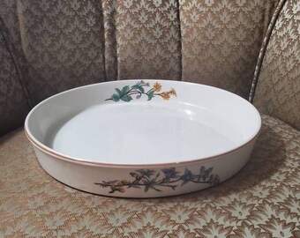 May include: White oval serving dish with floral patterns in green, yellow, and blue. The dish has a slightly raised rim and a light brown edge. The floral design is on the side of the dish. The dish is empty.