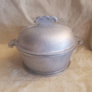 May include: A silver aluminum covered casserole dish with a textured surface and a handle on the lid.