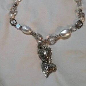 May include: A white pearl and crystal necklace with a silver charm of two intertwined hearts.