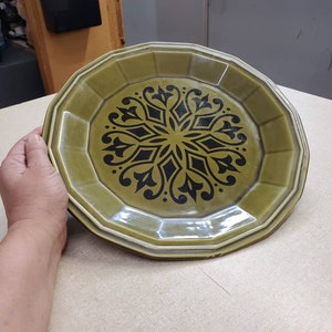 Könnte beinhalten: Ein grüner Keramikteller mit einem schwarzen und weißen geometrischen Muster. Der Teller hat einen gewellten Rand.