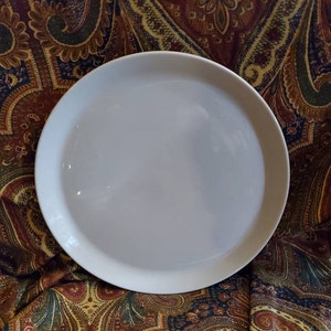 May include: A white ceramic serving platter with a slightly raised rim. The platter is round and has a smooth, glossy finish.