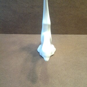 May include: A white ceramic bunny figurine in a yoga pose, with its head touching the ground and its body upright. The bunny is on a brown surface. The figurine has a smooth, glossy finish and a minimalist design.