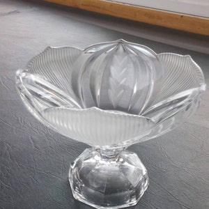 May include: A clear glass bowl with a fluted design and a pedestal base. The bowl is shaped like a flower with a central dome.