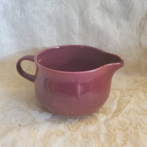 May include: A deep burgundy ceramic creamer or gravy boat with a rounded body and a single handle.