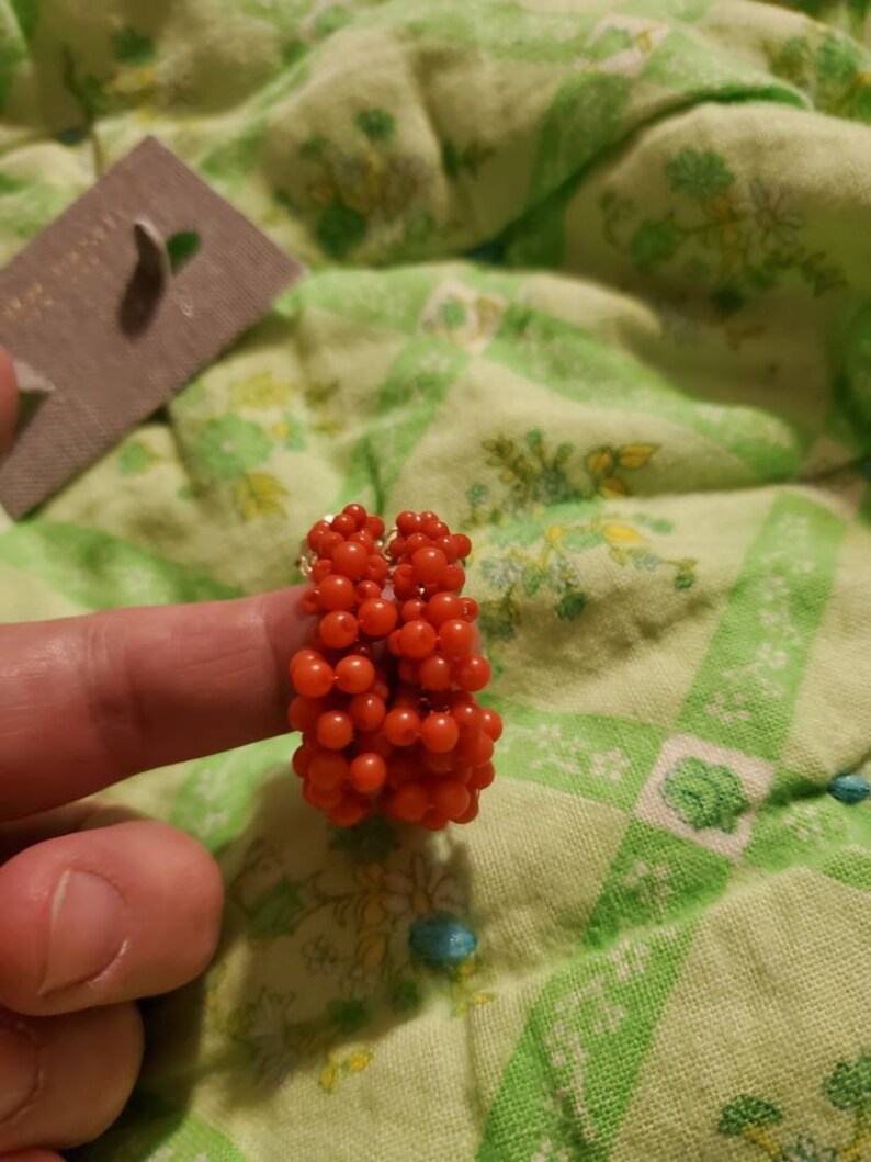 May include: A pair of red beaded hoop earrings. The earrings are made of small, round beads that are clustered together to form a hoop shape.
