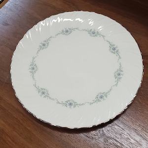 May include: A white ceramic plate with a gold rim and a delicate floral design in shades of green and blue.