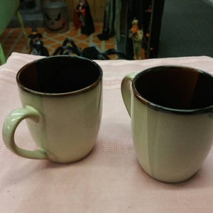 Peut inclure: Deux tasses à café en céramique avec un glaçage brun et blanc. Les tasses ont une forme arrondie et une large poignée.