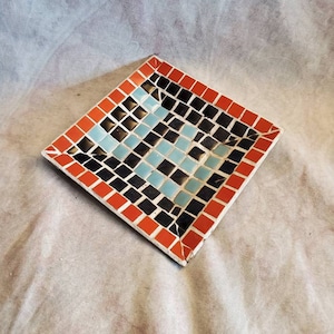 May include: A square mosaic tile tray with a red border and a black and blue mosaic design in the center.