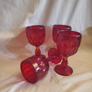 May include: Four red glass goblets with a textured design. The goblets are on a white fabric surface.