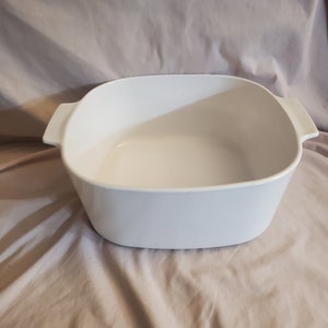 Puede incluir: Plato para hornear de cerámica blanca con dos asas. El plato está vacío y tiene un acabado liso y brillante.