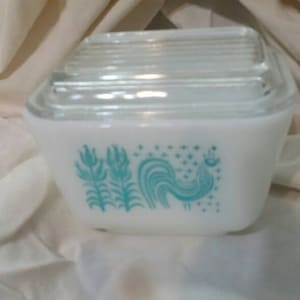 Puede incluir: Contenedor de almacenamiento de cerámica blanca con un gallo azul y un diseño floral. El contenedor tiene una tapa de vidrio transparente.