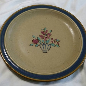 May include: A beige ceramic dinner plate with a blue rim and a floral design in shades of pink, green, and blue.