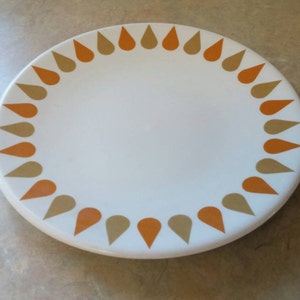 May include: A white ceramic plate with a brown and orange teardrop design around the edge.