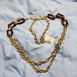 Pode incluir: Um colar de corrente de ouro com um detalhe de tartaruga marrom e dourado. O colar é em camadas e tem uma etiqueta de preço.
