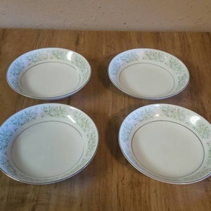 May include: Four white ceramic bowls with a green floral pattern. The bowls are all the same size and shape.