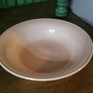 Op de afbeelding: Een lichtroze keramische kom met een geribbeld ontwerp. De kom is leeg en staat op een houten oppervlak.