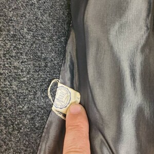 May include: A close-up of a gray wool coat with a label that reads "National Coat and Suit Industry" and "Dry Clean Only".