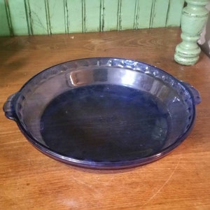 Op de afbeelding: Een blauwe glazen taartvorm met een gegolfde rand en twee handvatten.