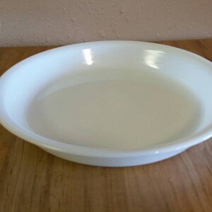 May include: A white ceramic pie dish, also known as a baking dish, on a wooden surface.