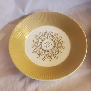 May include: A yellow and white ceramic plate with a brown floral design. The plate has a scalloped edge and a raised rim.