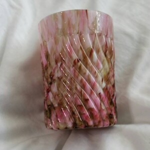 May include: A pink and brown swirl glass candle holder. The glass is clear and has a swirl pattern of pink and brown.