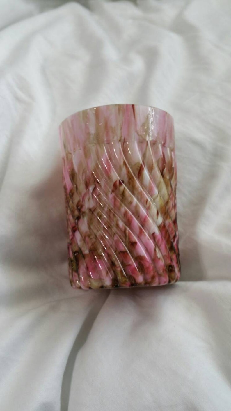 May include: A pink and brown swirl glass candle holder. The glass is clear and has a swirl pattern of pink and brown.