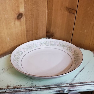 May include: A white ceramic bowl with a green and gold floral pattern around the rim.