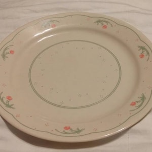 Puede incluir: Un plato de cena de cerámica blanca con un borde festoneado y un diseño floral en tonos verdes y rosas.