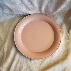 Op de afbeelding: Een grote, ronde, perzikkleurige keramische plaat met een verhoogd, concentrisch ringontwerp rond de rand.