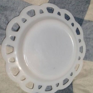 May include: White milk glass plate with a scalloped edge and a decorative cut-out design. The plate is on a blue and white checkered fabric.