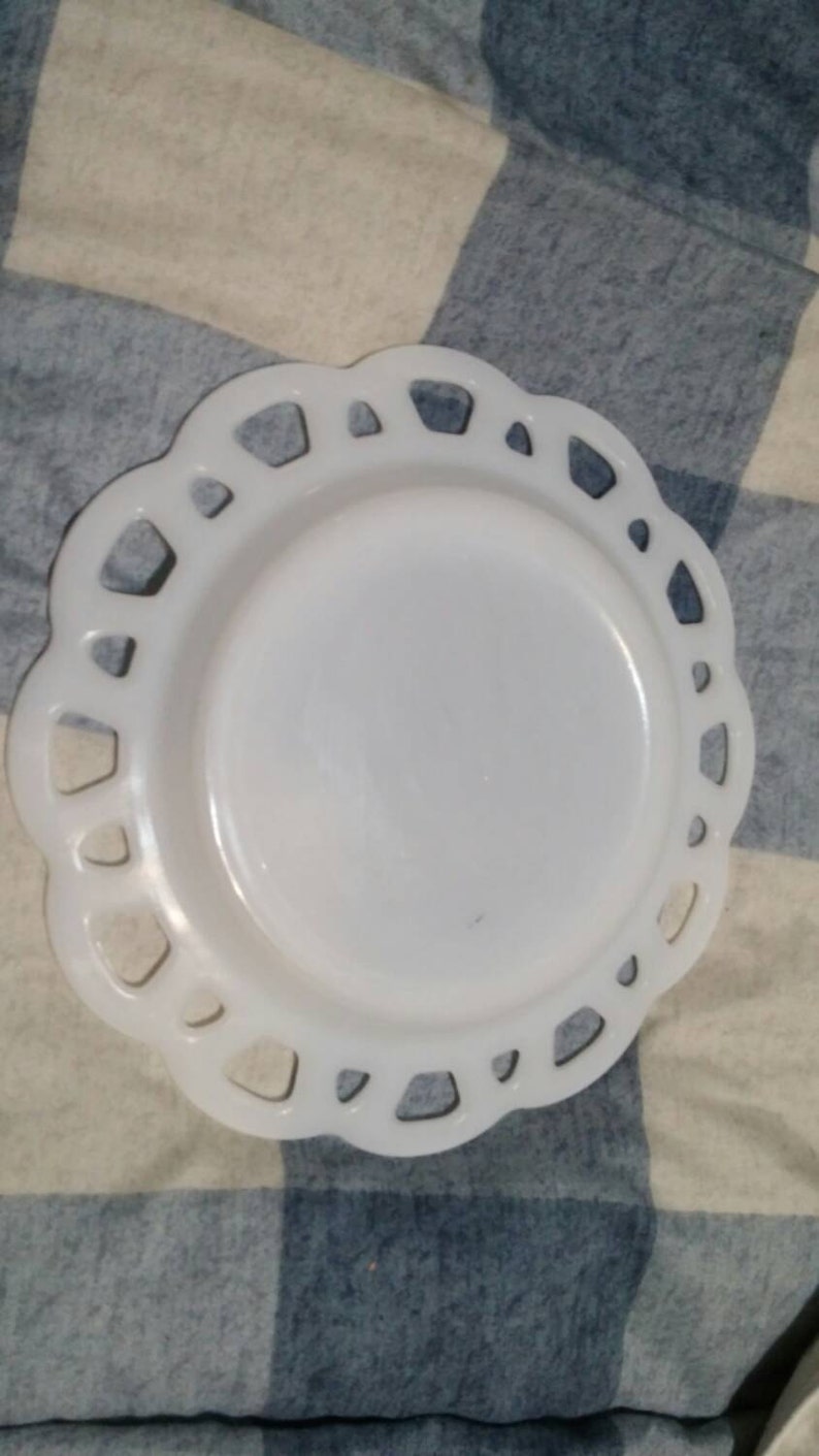 May include: White milk glass plate with a scalloped edge and a decorative cut-out design. The plate is on a blue and white checkered fabric.